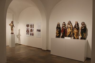 Ausstellungsraum mit fünf weiblichen Skulpturen im Vordergrund und einer männlichen Figur im Hintergrund.