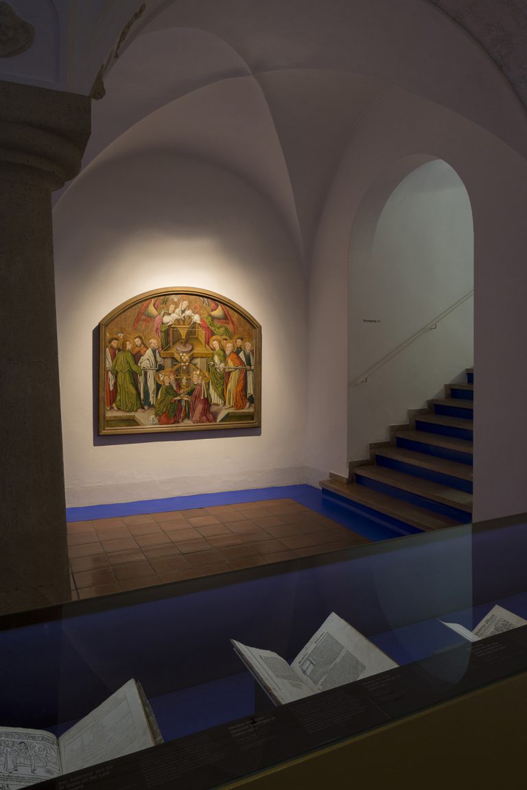 Ausstellungsraum, im Vordergrund eine Vitrine mit Büchern, im Hintergrund ein Gemälde.