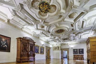 Farbfotografie: Raumansicht eines großen prächtigen Raums mit Holzboden, weißen Wänden und stuckverzierter Decke