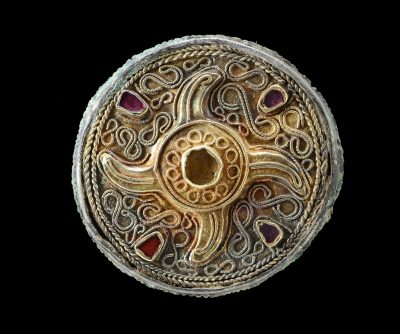 Eine kreisrunde Fibel mit filigraner Verzierung und violett schimmernden Glaseinlagen.