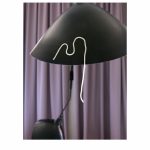 Fotografie: Eine gelbe Nudel hängt an einem schwarzen Lampenschirm vor einem lila Vorhang.