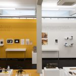 Foto: Ansicht des Ausstellungsraums. An einer gelben und weißen Wand hängen Vitrinen.