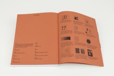 Farbfoto: Ein aufgschlagenes Buch liegt auf einem weißen Hintergrund. Zu sehen ist eine orangefarbene aufgeschlagene Doppelseite.