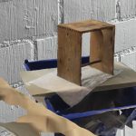 Farbiges Rendering: Ein Ulmer Hocker aus hellem Holz scheint auf einer Platte vor einer weißen Backsteinwand zu schweben