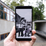 Farbfoto: Detailaufnahme eines Smartphones, das eine Hand vor das Gebäude der Hochschule für Gestaltung Ulm hält. Auf dem Display ein Schwarzweiß-Foto mit einer historischen Aufnahme am gleichen Ort