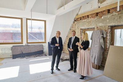 Farbfoto: Blick in den Innenraum im Dachstuhl. Drei Personen, darunter eine Frau und zwei Männer, stehen in der Mitte.