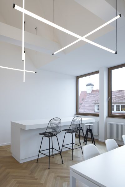Farbfoto: Blick in einen hellen Innenraum im Dachgeschoss mit weißen Tischen und Stühlen
